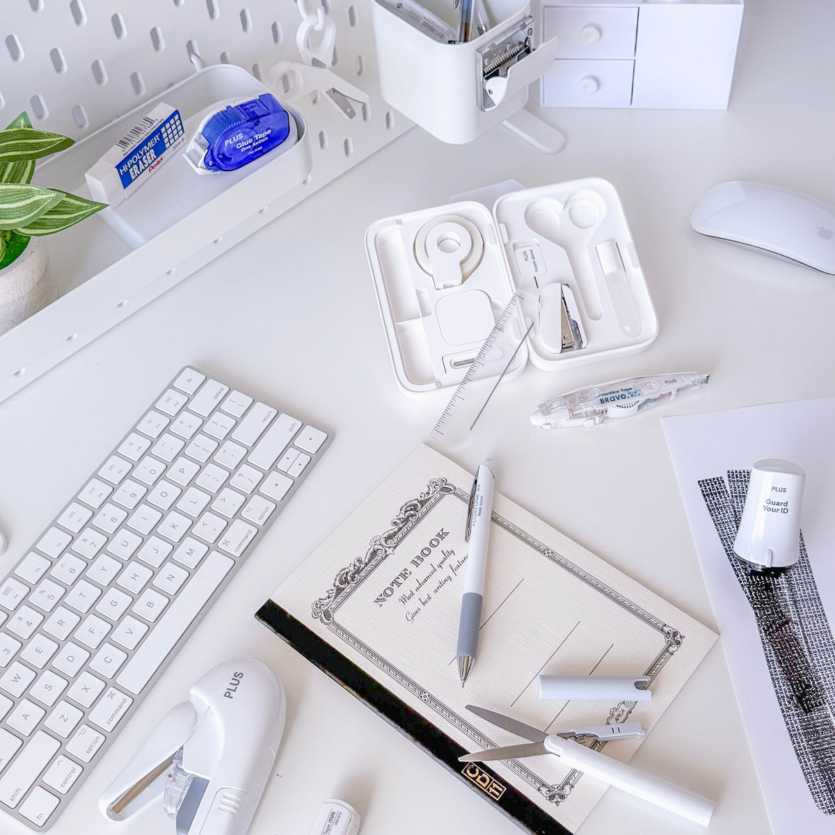 White desk workspace with a keyboard mouse notebook pens ruler correction tape and an open case of small stationery tools
