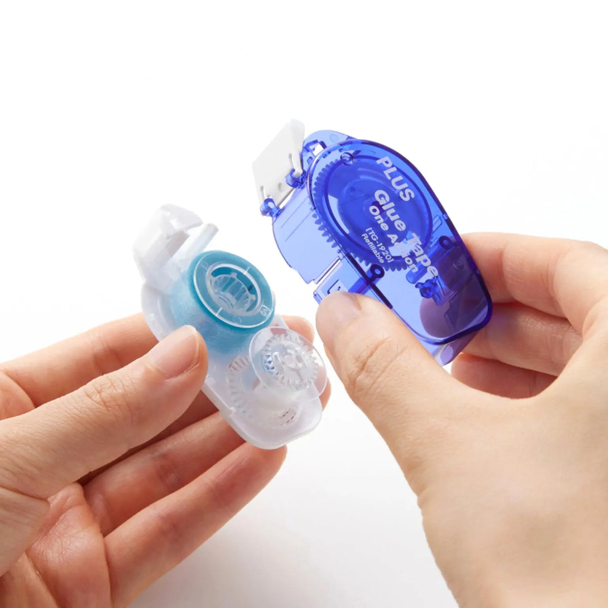 Hands demonstrate a translucent refill for a blue PLUS One Action permanent glue tape applicator designed for smooth permanent bonding