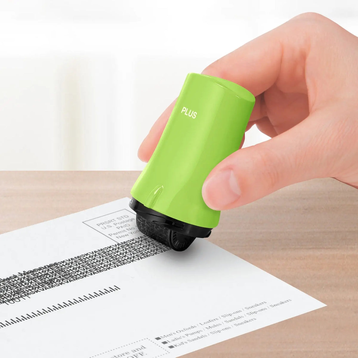 Hand using a green privacy roller stamp to cover personal information on a printed document at a desk en dash?