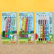Three colorful Peanuts themed Pentel pen packages displayed on a yellow and wood grain background, including liquid gel and ballpoint pens in assorted colors