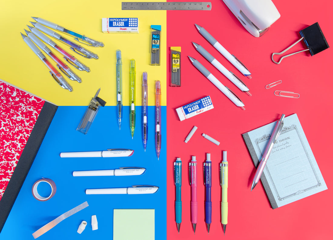 Flat lay of assorted pens pencils markers erasers and correction supplies arranged on blue red and yellow backgrounds with paper clips notebooks and tape beside them