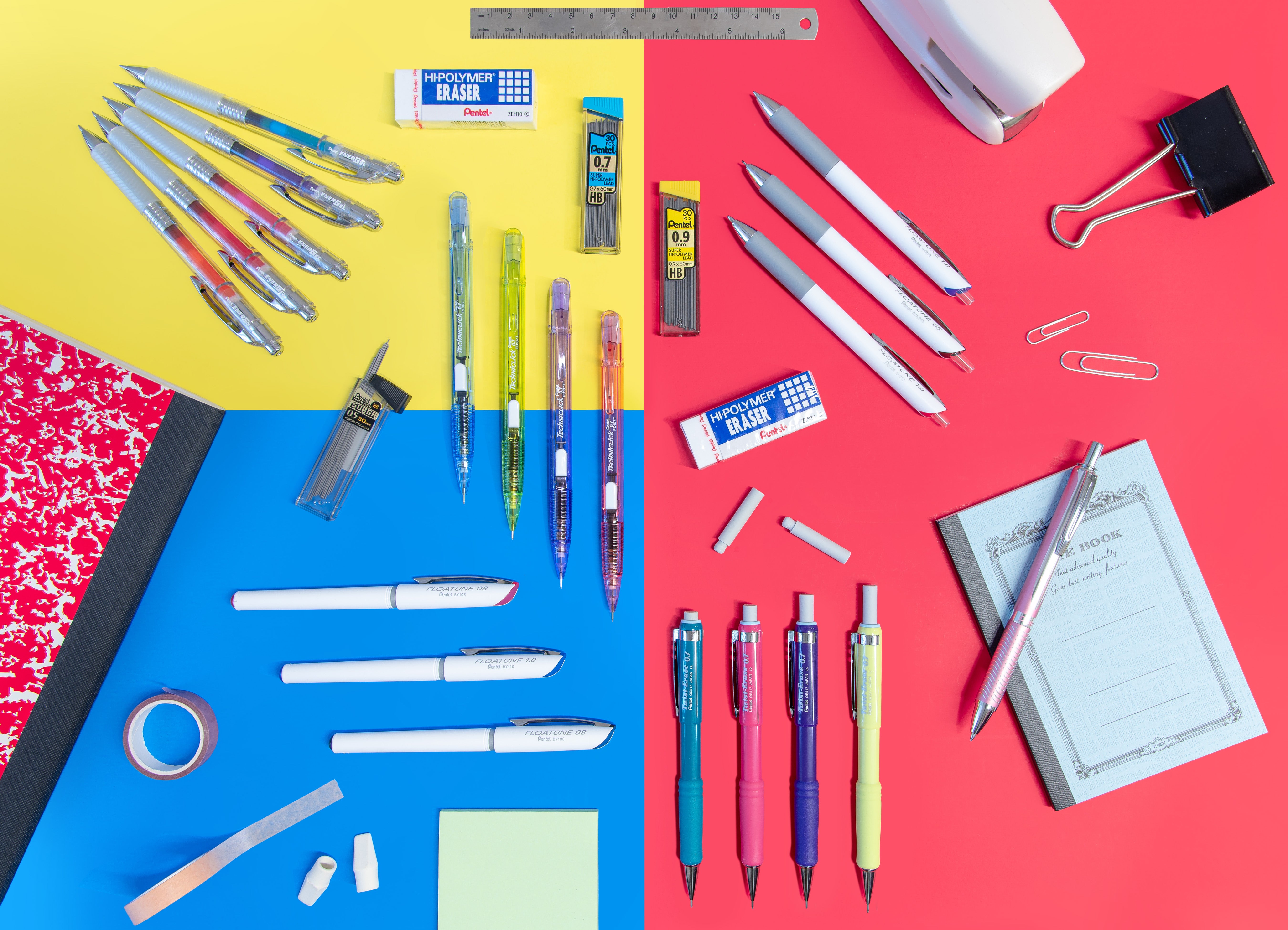 Flat lay of assorted pens pencils markers erasers and correction supplies arranged on blue red and yellow backgrounds with paper clips notebooks and tape beside them