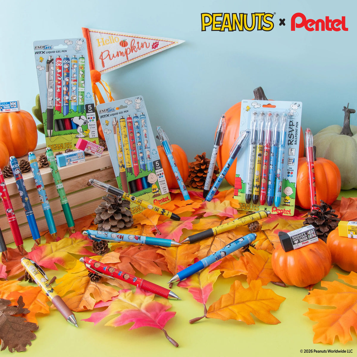 Autumn-themed arrangement of colorful pens and writing instruments among pumpkins, pinecones, and fall leaves, with Peanuts and Pentel logos in the background