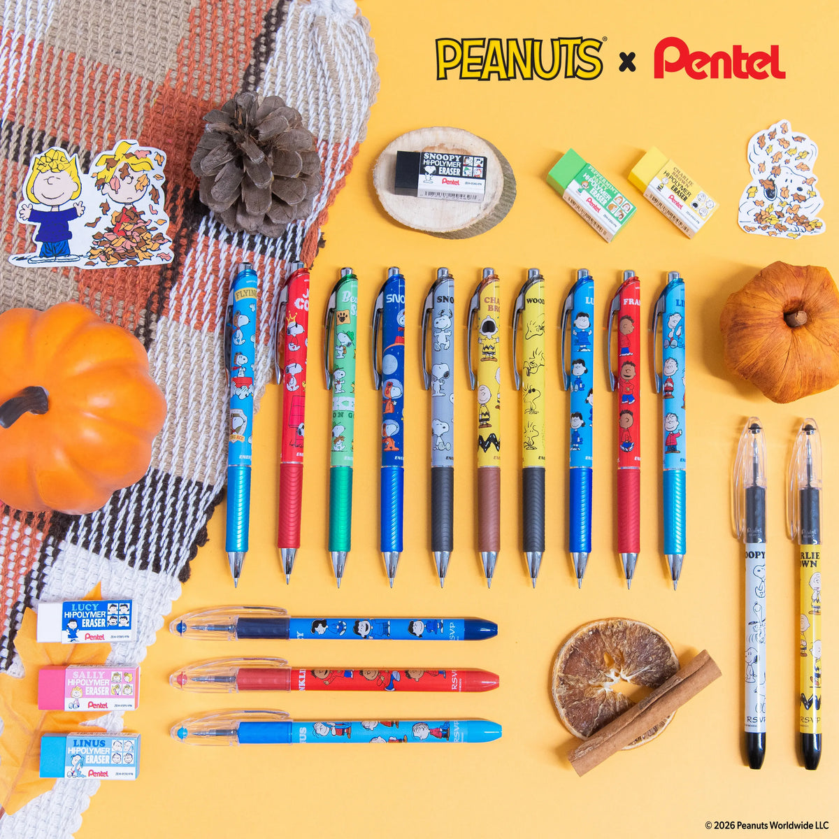Peanuts and Pentel pens pencils erasers and correction tape arranged on a yellow background with autumn pumpkins pinecone and dried leaves