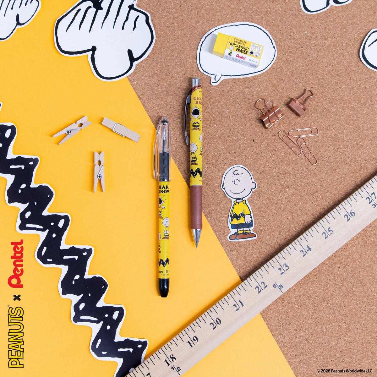 Flat lay of yellow and brown pens, paper clips, mini clothespins, a ruler, and Peanuts character stickers on yellow paper and a corkboard surface