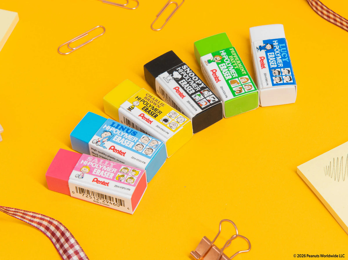 Six assorted PEANUTS and Pentel Hi Polymer erasers in pink blue yellow black green and white wrappers arranged on a bright yellow desk