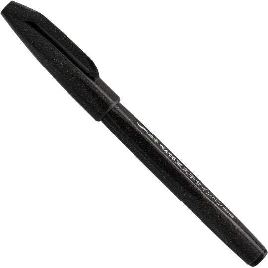 Pentel Arts black brush tip pen shown diagonally on a white background for expressive lettering drawing and other art projects