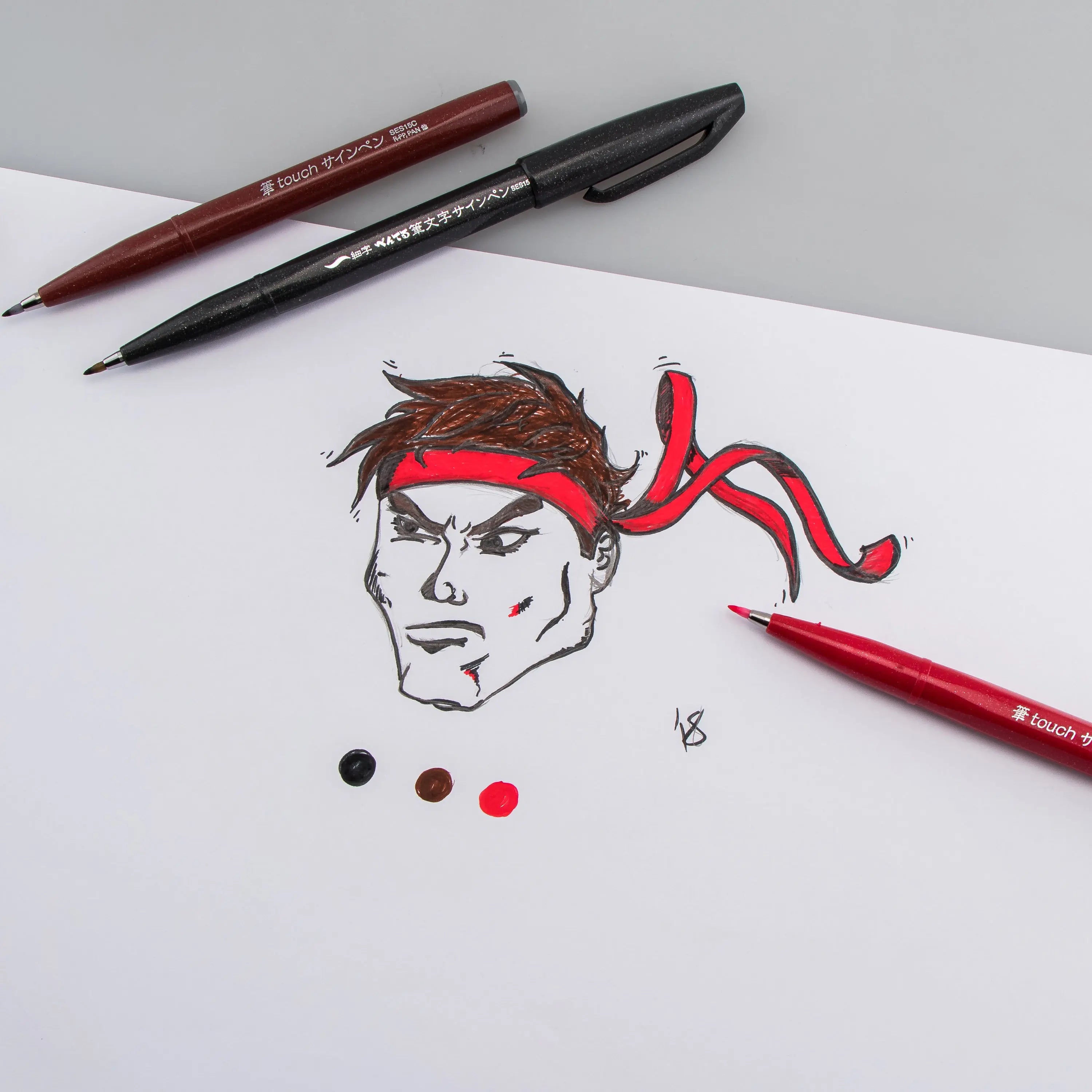 Pentel brush tip pens in black red and brown shown with an expressive ink drawing and colorful swatches on white paper for creative art supplies