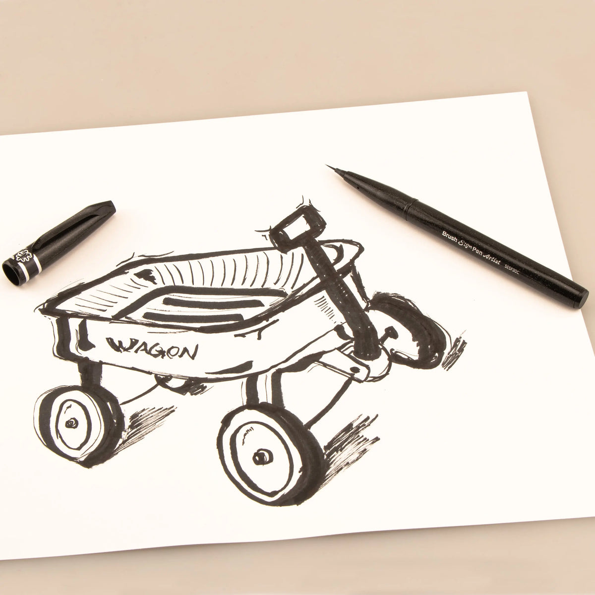 Black micro brush pen beside a detailed dragon wagon sketch on white paper showcasing expressive ink lines and precise art supplies control