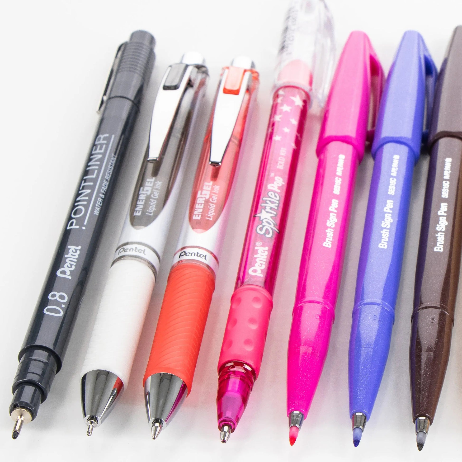 A collection of colorful writing instruments including gel pens, ballpoint pens, and brush sign pens arranged in a neat row, showcasing premium art supplies for creative journaling.