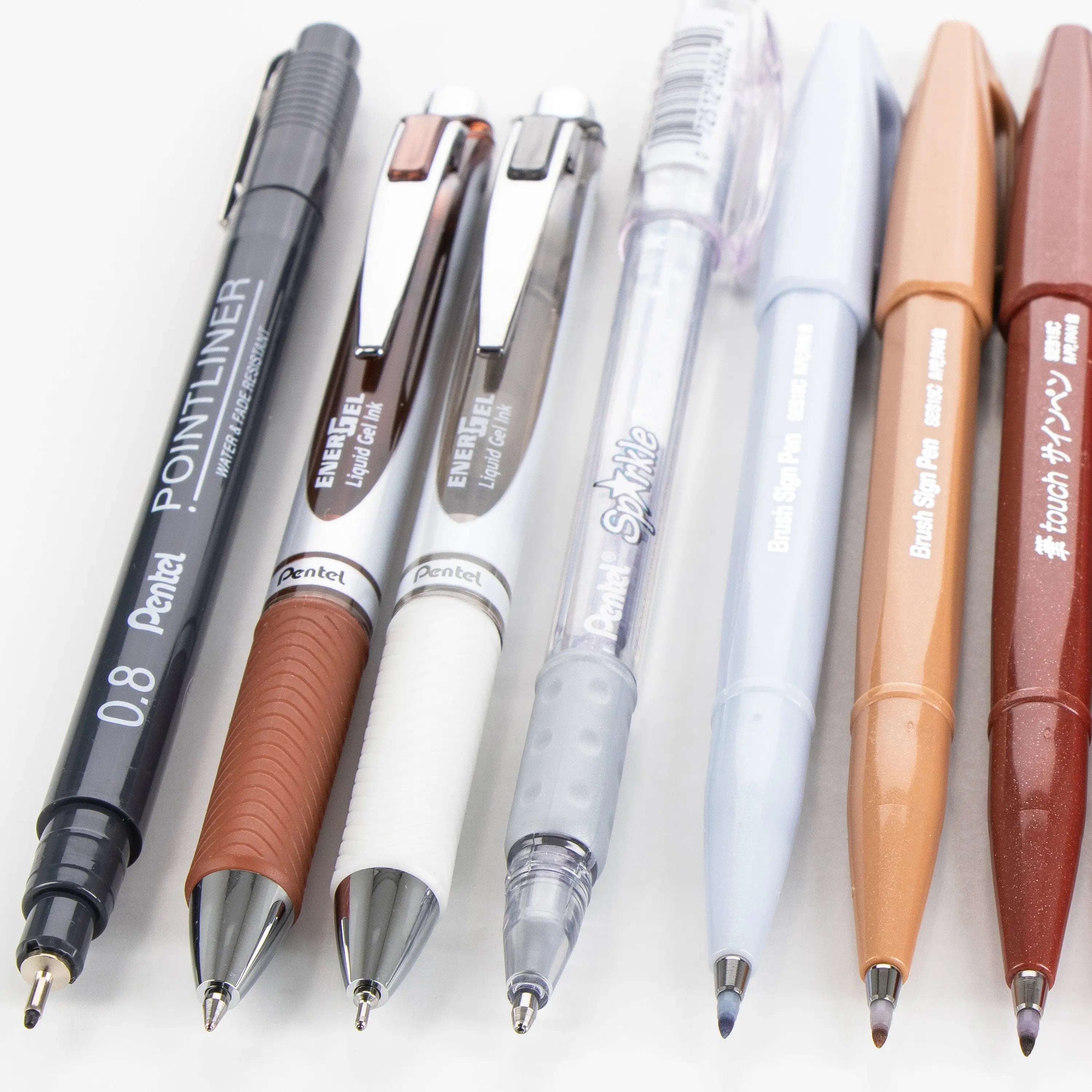 A selection of premium writing tools including ballpoint pens, gel pens, mechanical pencils, and correction pens in neutral tones designed for creative journaling and note-taking.