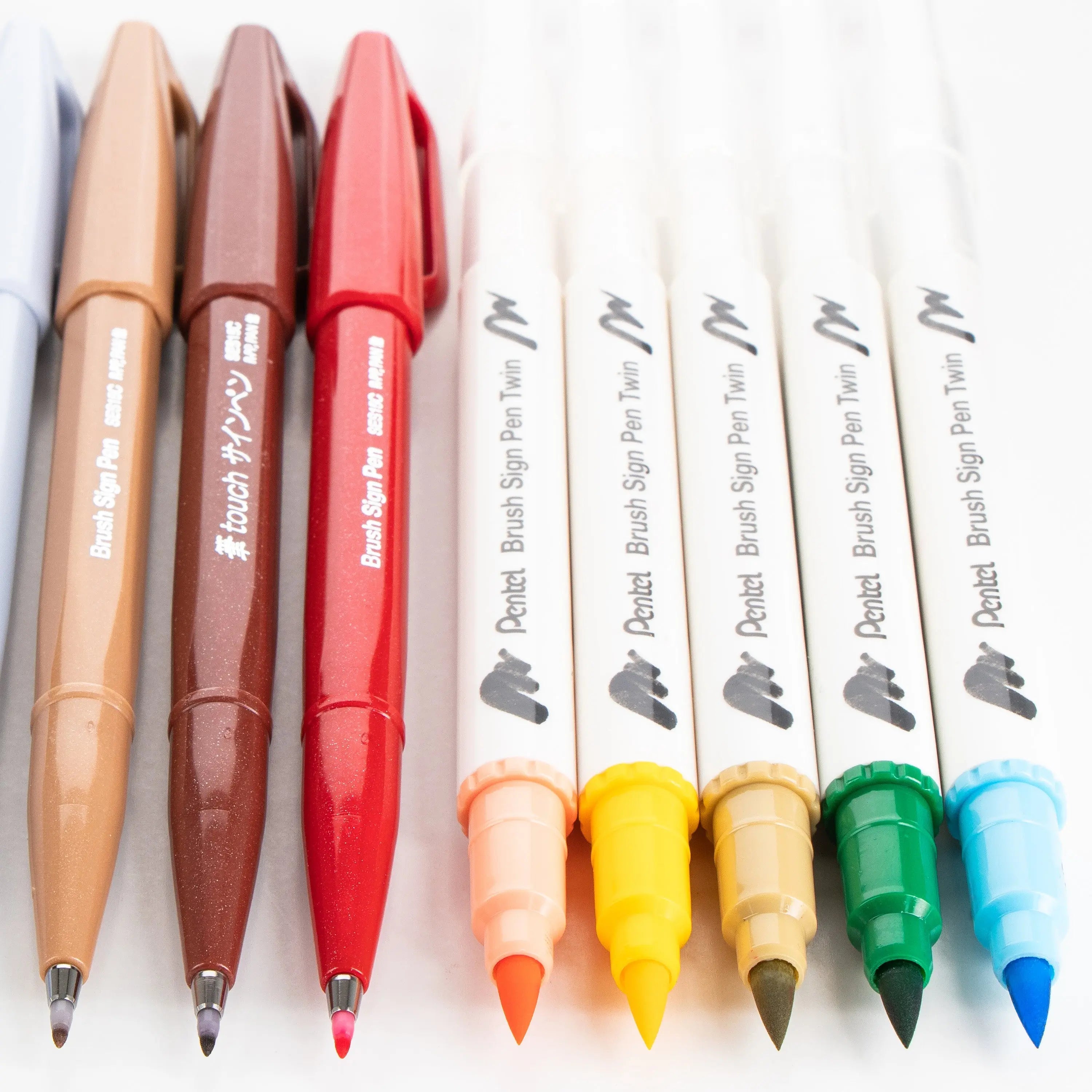 A set of colorful brush and ballpoint pens arranged in a row, featuring warm and cool tones, ideal for creative journaling and artistic expression.