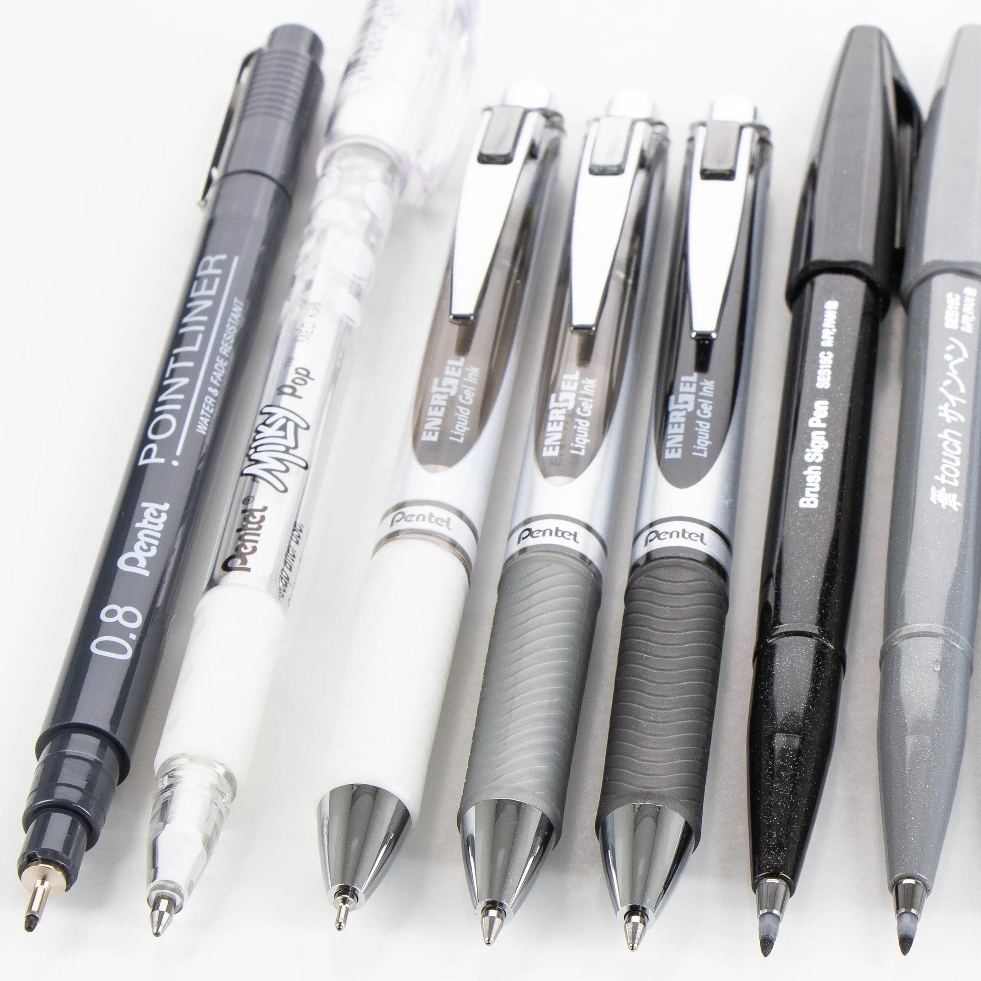 Close-up of a variety of Pentel pens and mechanical pencils with sleek silver clips and textured grips, showcasing premium writing tools ideal for journaling and creative expression.