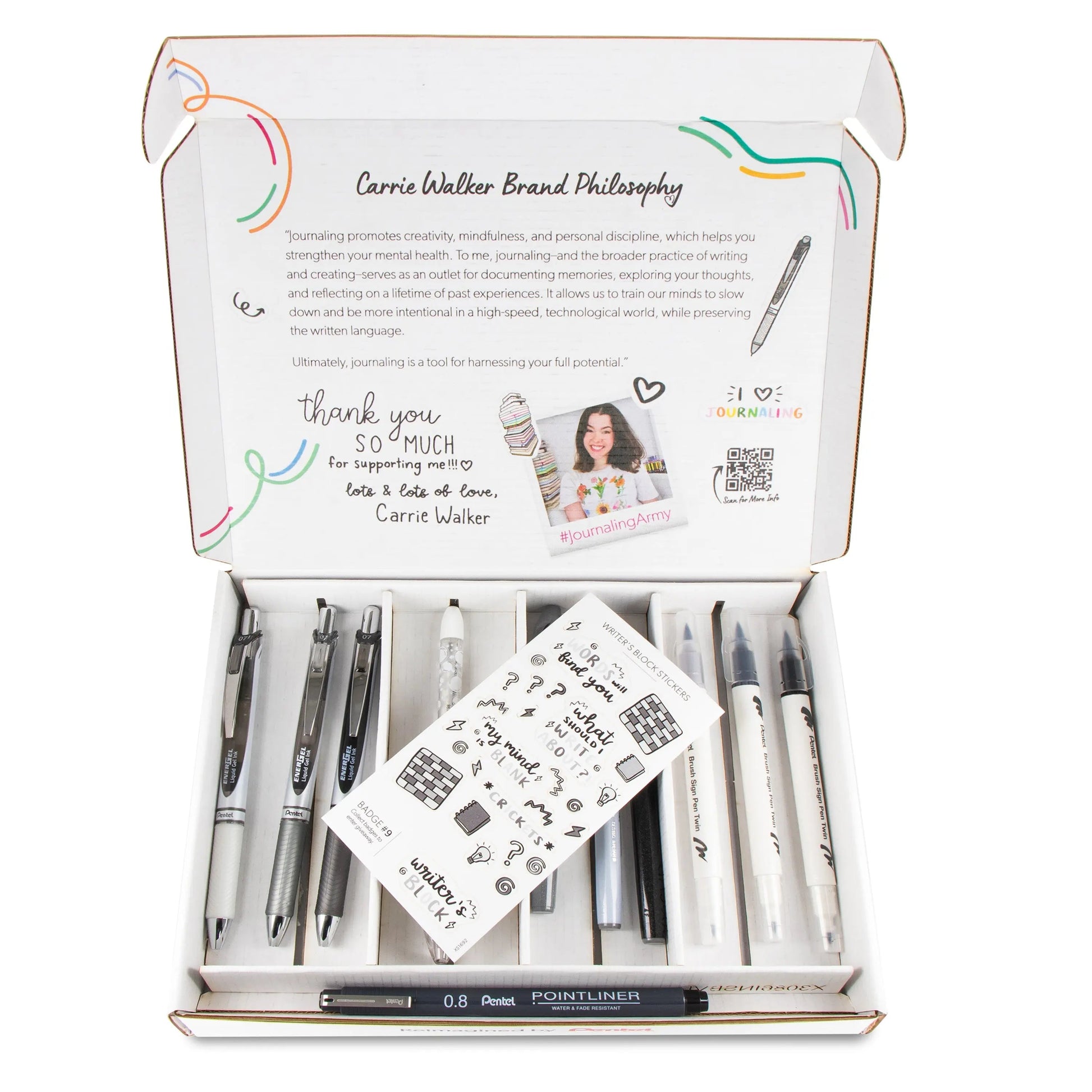 Open box displaying a set of sleek black and white writing tools including pens, markers, and a mechanical pencil arranged neatly, accompanied by a small sheet of journaling-themed stickers and a printed note expressing creative inspiration.