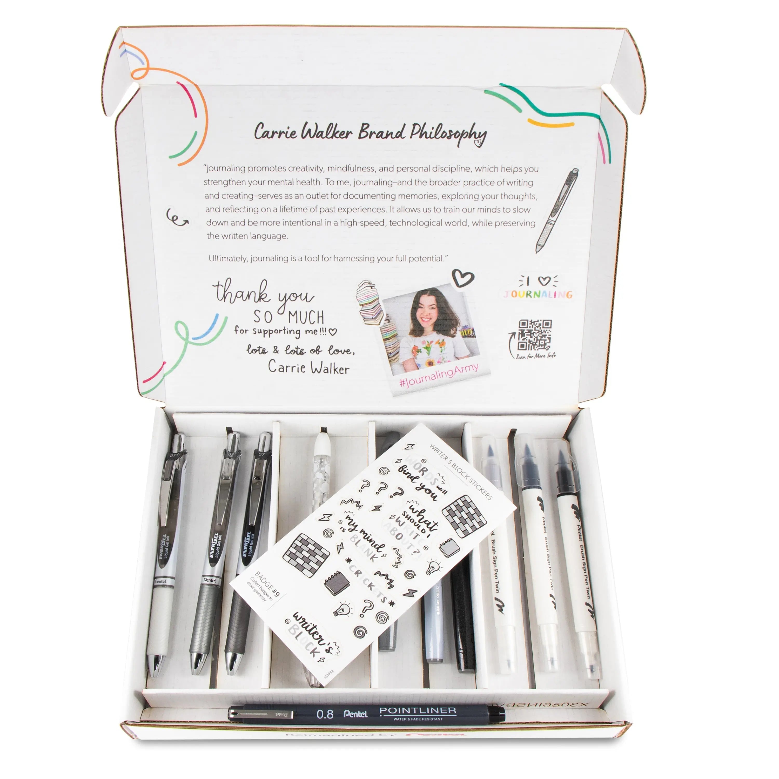 Open box displaying a set of sleek black and white writing tools including pens, markers, and a mechanical pencil arranged neatly, accompanied by a small sheet of journaling-themed stickers and a printed note expressing creative inspiration.
